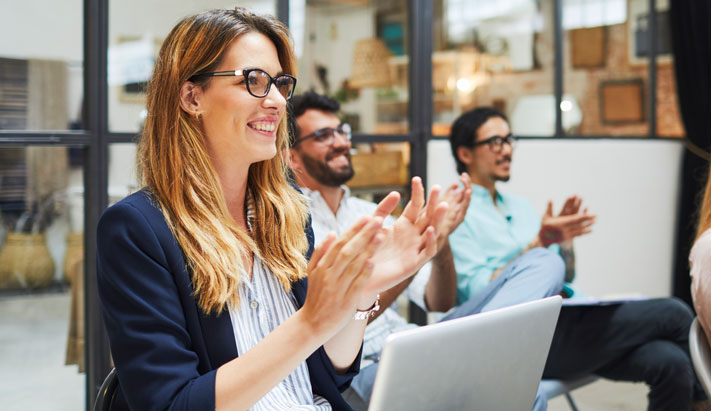 Three people in a meeting room smiling and clapping